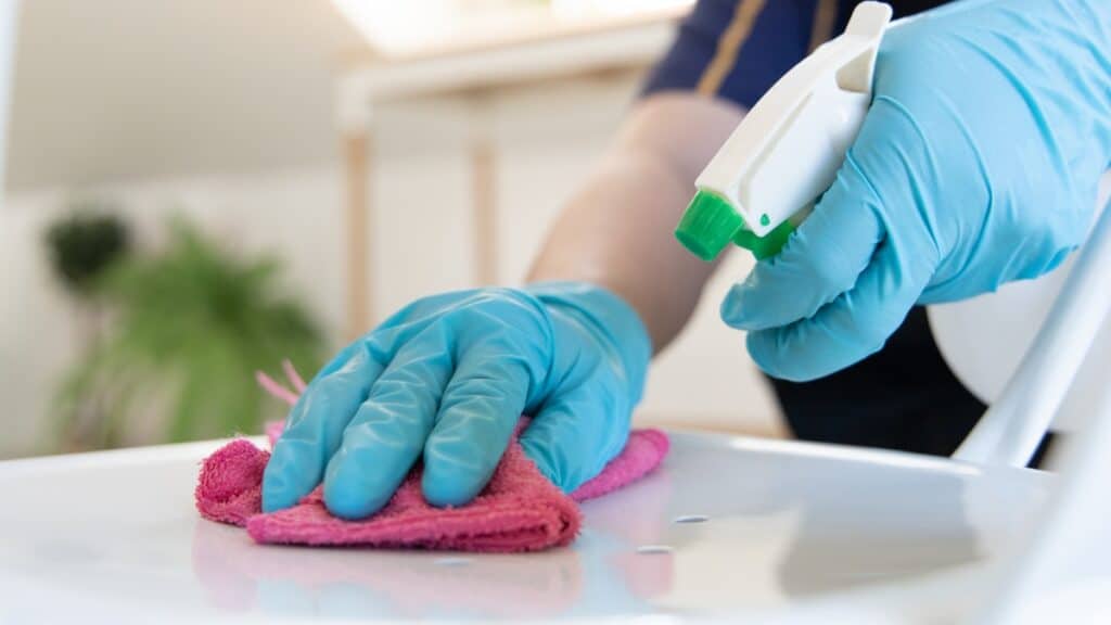 Home cleaning team using disinfectant spray in a kitchen.